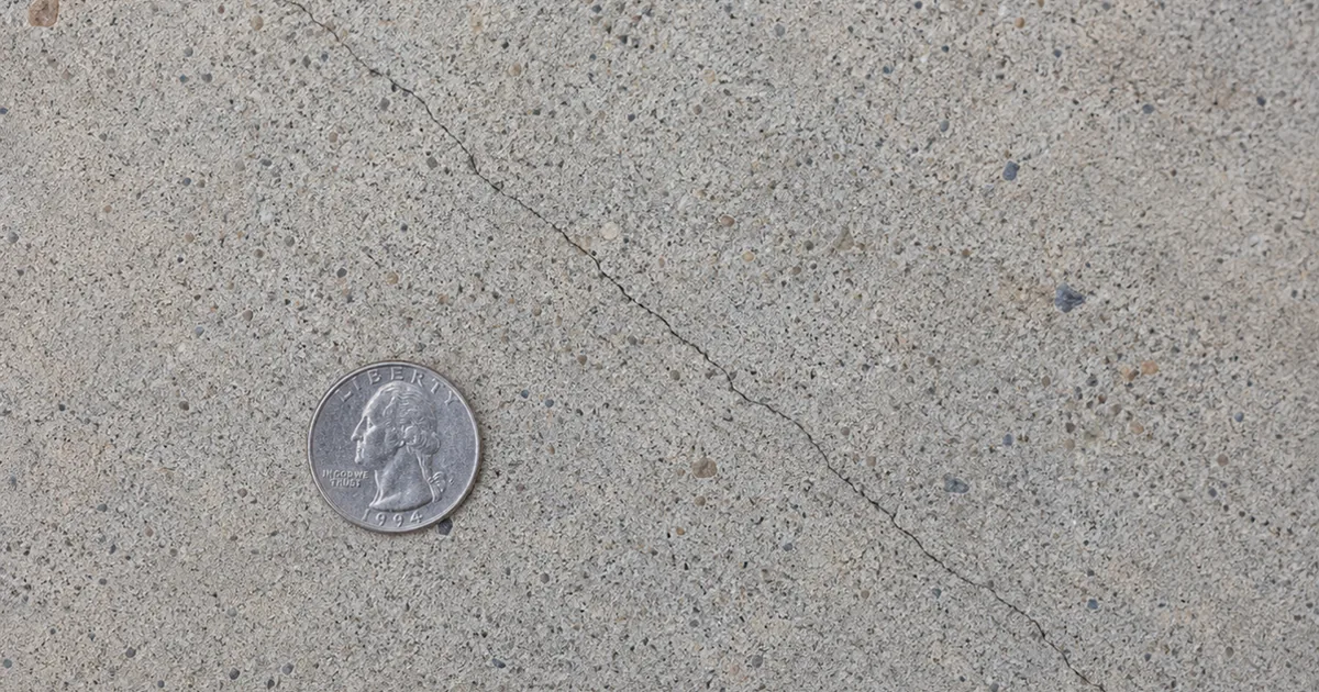Hairline diagonal crack across a residential concrete slab foundation with a coin placed for scale