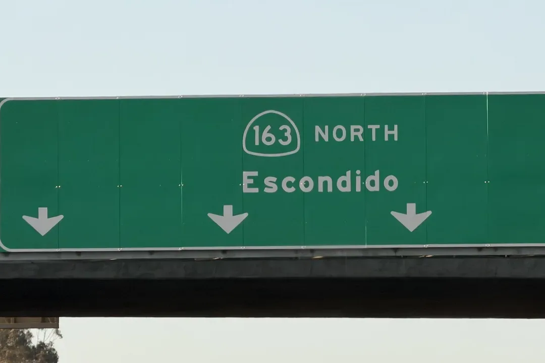 Green overhead sign for State Route 163 North to Escondido with down arrows over the freeway lanes
