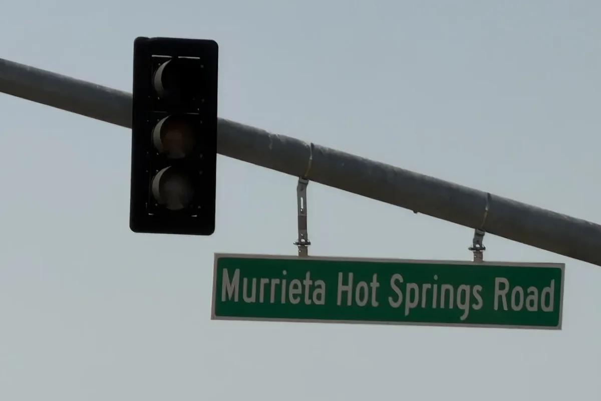 Green Murrieta Hot Springs Road street sign hanging from a traffic signal arm beside a signal head